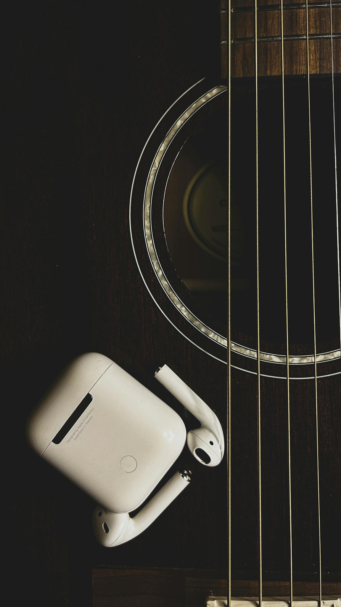 A close-up shot of an acoustic guitar body with wireless earbuds placed on it.