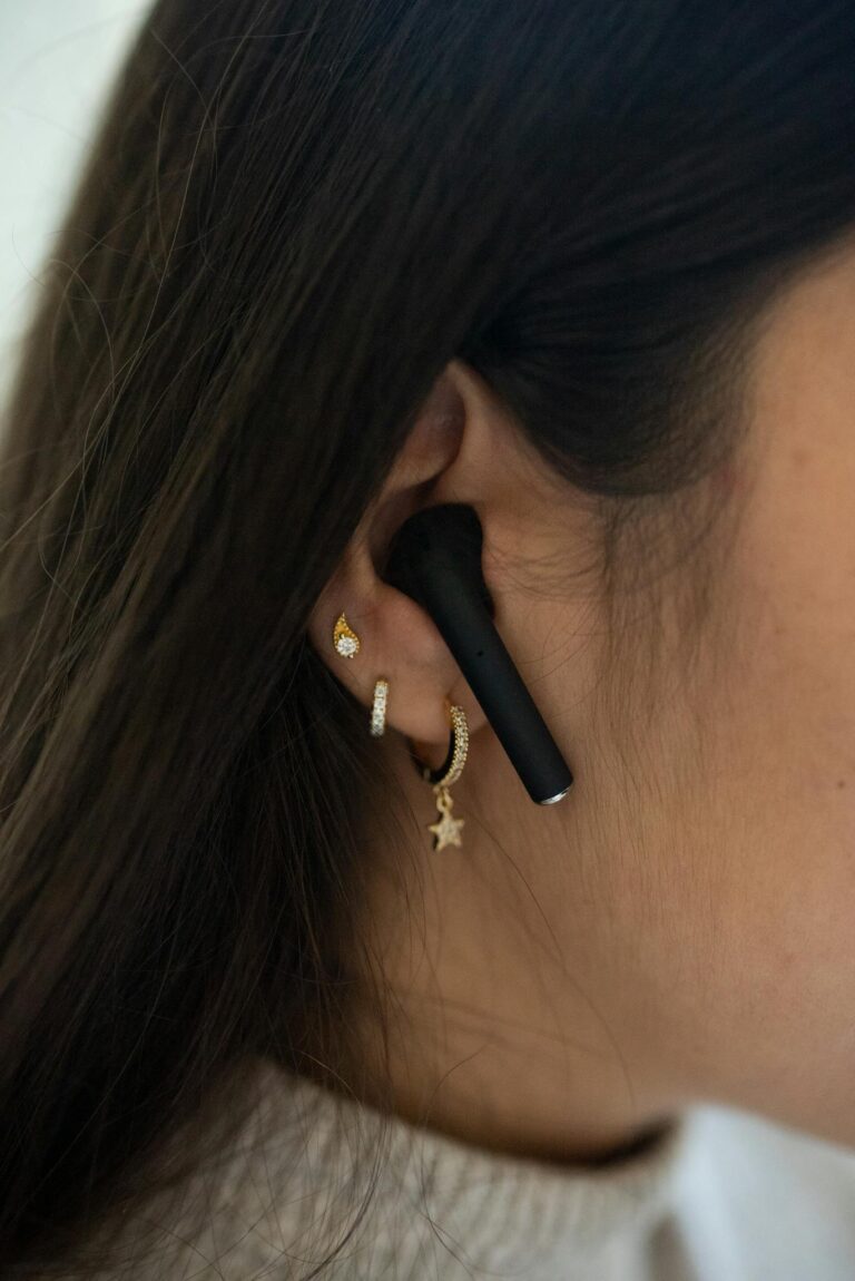 A detailed close-up image of an ear adorned with earrings and a black wireless earbud, showcasing modern style.