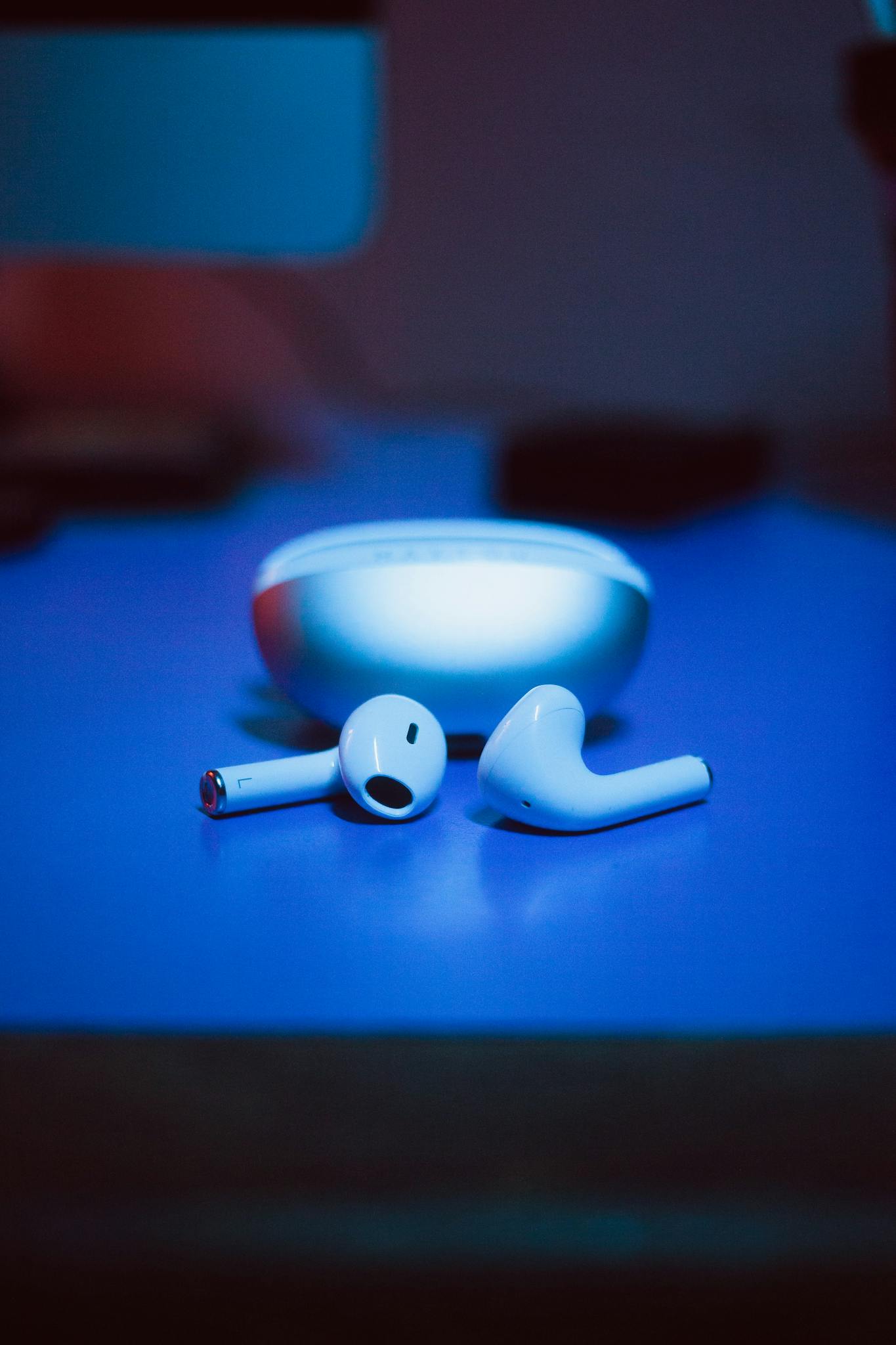 Close-up of white wireless earbuds with charging case on a blue-lit surface.