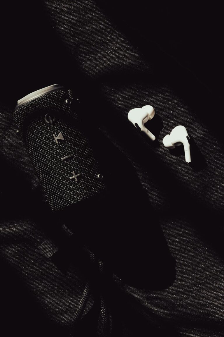 Stylish black speaker and white earphones arranged on a dark textured background, casting dramatic shadows.