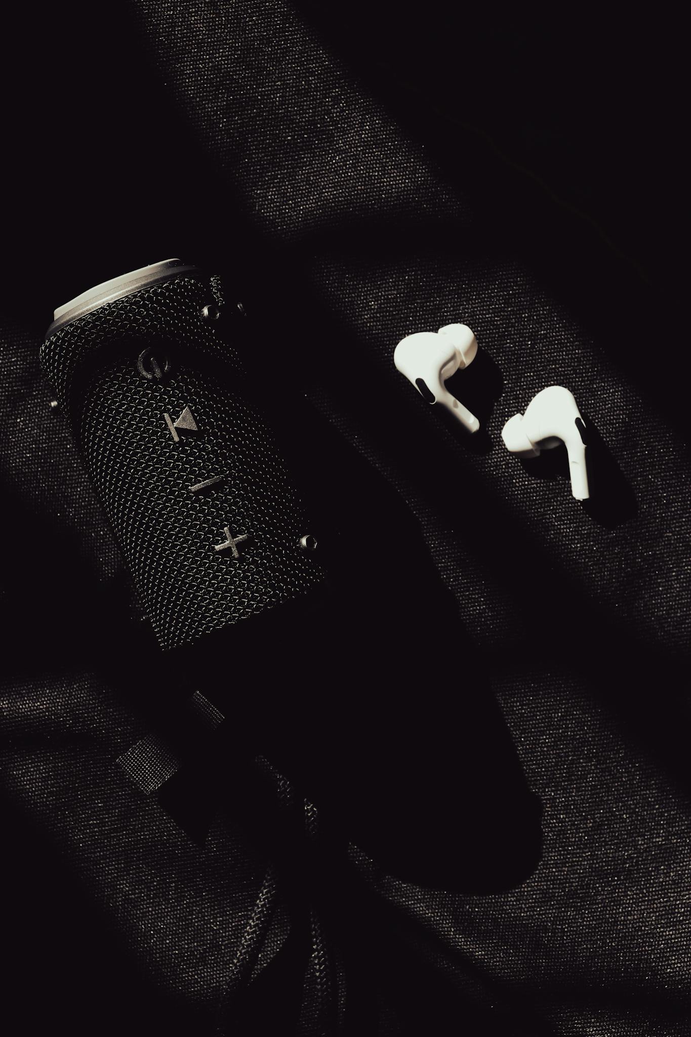 Stylish black speaker and white earphones arranged on a dark textured background, casting dramatic shadows.